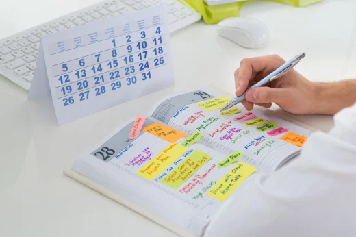 Close-up Of Businessman With Calendar Writing Schedule In Diary
