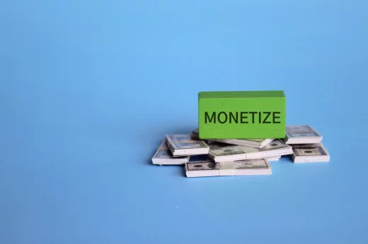 Wooden cube with text MONETIZE and banknotes on blue background