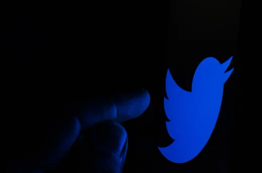 Twitter company logo on the smartphone screen in a dark room and a finger targeting at it