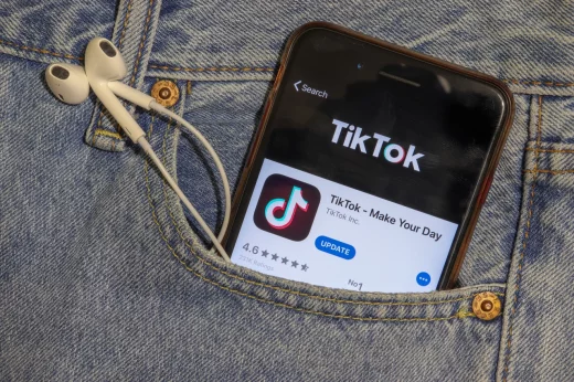 TikTok app icon on phone screen in blue jeans pocket with headphones