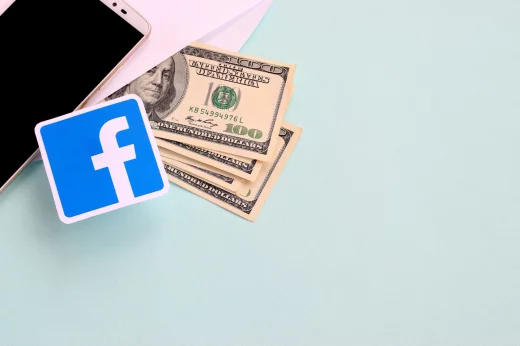 Facebook paper logo lies with envelope full of dollar bills and smartphone
