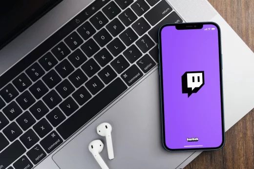 Twitch app on the smartphone screen on wooden background with a computer beside it