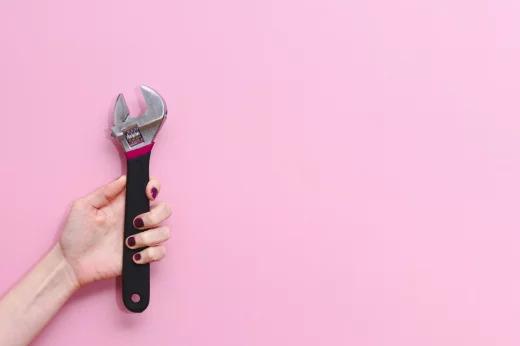 Young woman holding an adjustable monkey wrench tool on a pink background